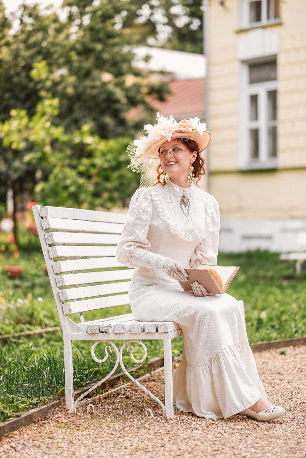A smiling red-haired woman in a vintage dress sitting on a garden bench with a book, illustrative photograph